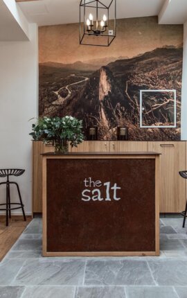 Ein stilvoller Empfangsbereich im the salt townhouse mit Holzmöbeln und einem großen Wandbild, das eine Berglandschaft zeigt.