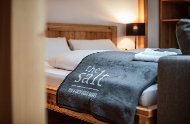Gemütliches Hotelzimmer mit Doppelbett, Holzrahmen und grauer Decke mit Aufschrift "the salt"