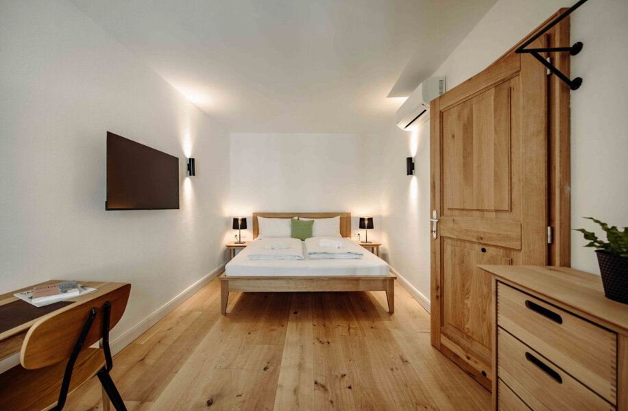 Modernes Zimmer mit Holzboden, Bett, Wand-TV, Schreibtisch und Pflanzen.