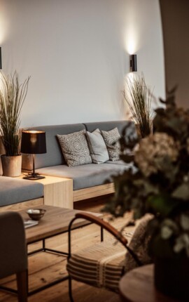 Cozy lounge area with a gray sofa, patterned cushions, and warm lighting. Natural decor elements create a relaxing atmosphere.