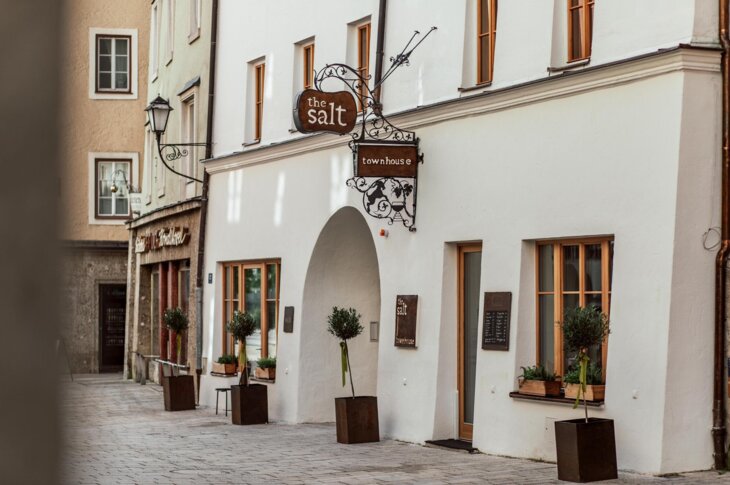 The salt townhouse exterior with potted plants, wooden windows, and decorative signage on a charming street.