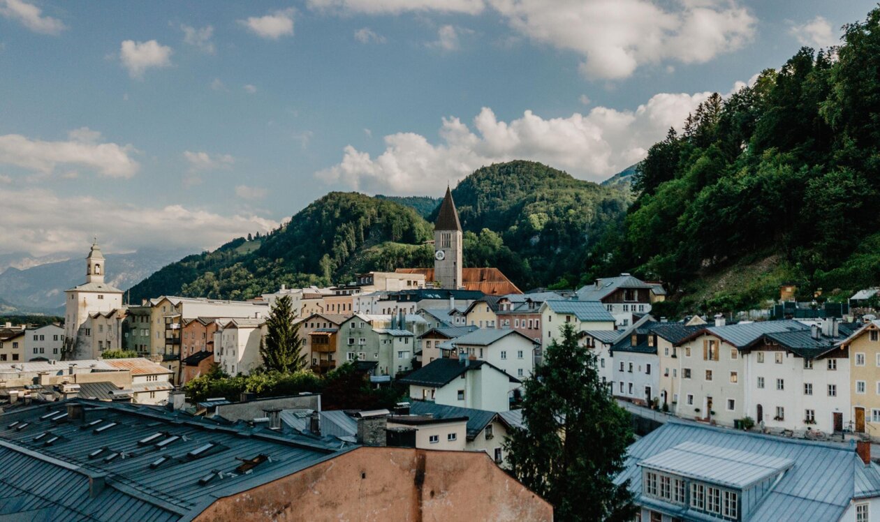 Stadtansicht von Hallein, umgeben von grünen Hügeln und einer Kirche mit Uhrturm im Zentrum unter blauem Himmel.