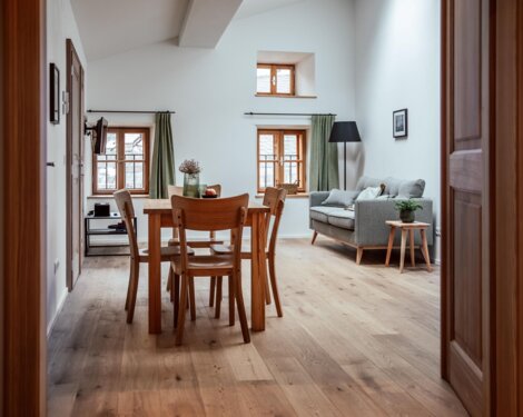 Heller Wohn- und Essbereich mit Holzboden, Esstisch, grauem Sofa und großen Fenstern.