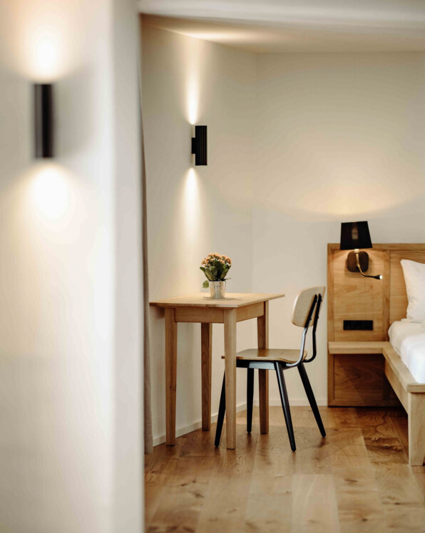 Gemütliches Zimmer mit Holztisch, Stuhl und Blumen, stilvoll beleuchtet.