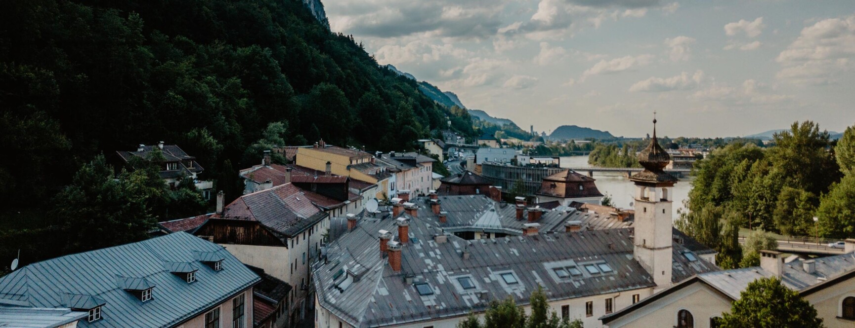 Blick auf Hallein mit historischen Gebäuden, bewaldeten Hügeln und Fluss unter einem bewölkten Himmel.