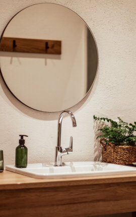 Warmer, minimalistischer Waschtisch mit rundem Spiegel, Holzmöbel und Pflanzen im Badezimmer.