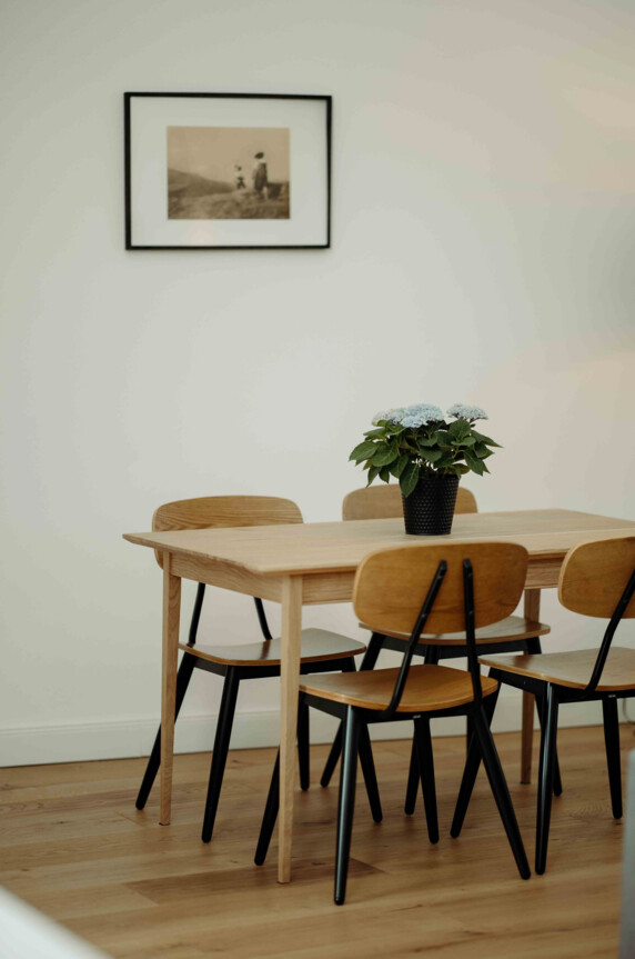 Moderner Holztisch mit vier Stühlen, darauf eine Vase mit Blumen; an der Wand ein gerahmtes Foto.