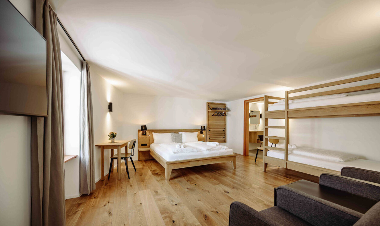 Spacious hotel room with a double bed, bunk beds, wooden flooring, and modern decor.