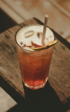 Iced drink with lime wedge and straw on a rustic wooden stool in warm sunlight.