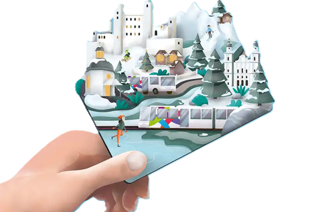 Hand hält Illustration einer winterlichen Alpenstadt mit Burgen, Tannen, Skifahrern und einem Regionalzug.