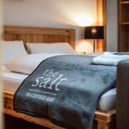 Gemütliches Hotelzimmer mit Doppelbett, Holzrahmen und grauer Decke mit Aufschrift "the salt"