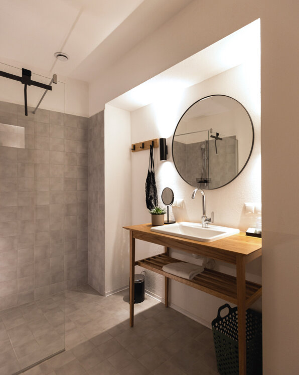 Modernes Badezimmer mit Holzwaschtisch, rundem Spiegel und begehbarer Dusche.