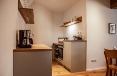 Voll ausgestattete Küche mit Kaffeemaschine, Ofen und Holzregalen in einem the salt-Apartment.