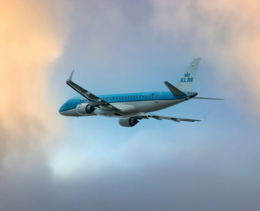 A KLM airplane flying through a cloudy sky with a serene sunset backdrop.