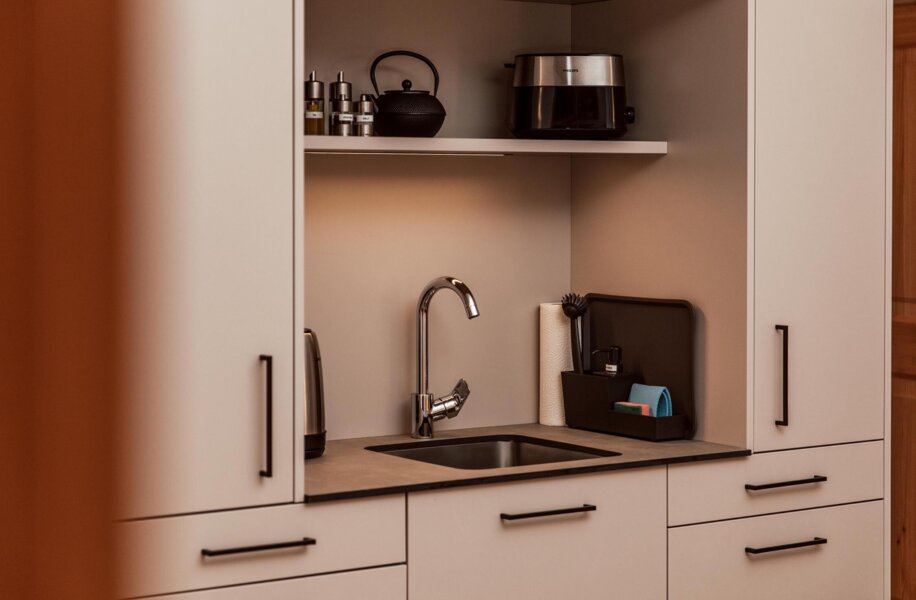 Moderne Küchenzeile mit Waschbecken, Wasserkocher, Toaster und Teekanne auf einem Regal.