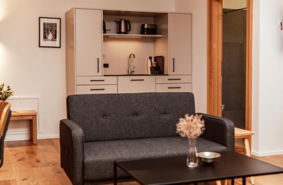 Juniorsuite im the salt townhouse mit grauem Sofa, stilvollem Tisch und Küchenzeile.