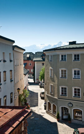 Straßenszene in Hallein mit historischen Gebäuden und Bergen im Hintergrund bei klarem Himmel.