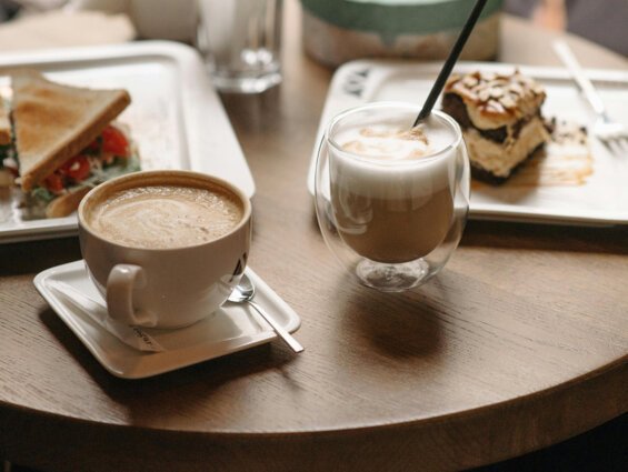 Cappuccino and latte on a café table with a toasted sandwich and a slice of cake.