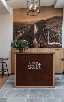 Ein stilvoller Empfangsbereich im the salt townhouse mit Holzmöbeln und einem großen Wandbild, das eine Berglandschaft zeigt.
