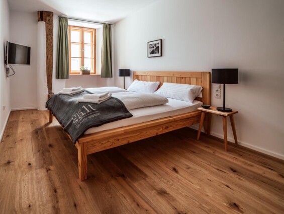 Gemütliches Schlafzimmer mit Holzboden, Doppelbett, TV und Fenster mit grünen Vorhängen in einer modernen Unterkunft.