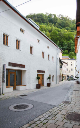 Eine ruhige, gepflasterte Straße mit weißen Gebäuden und grüner Hügellandschaft im Hintergrund in Hallein.
