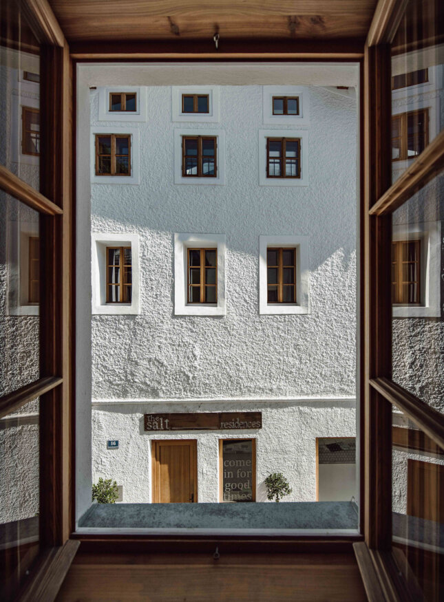 Blick aus einem Fenster auf the salt residences mit Holzfenstern. Ein Schild über der Tür weist auf "the salt residences" hin.