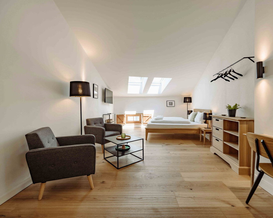 Helles, modernes Zimmer mit Holzfußboden, Sitzbereich, Bett und Dachfenster.