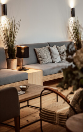 Cozy lounge area with a grey sofa, decorative pillows, plants, and soft lighting.
