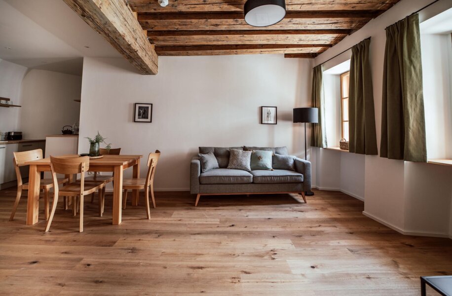 Wohnbereich mit Holzboden, grauem Sofa, Esstisch und einer voll ausgestatteten Küchenzeile. 