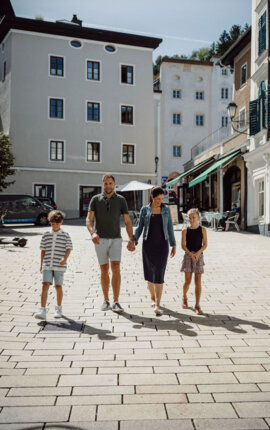 Family strolling through Hallein’s old town on a sunny day, walking past cafés and historic townhouses.