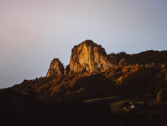 Die Barmsteine bei Sonnenaufgang mit herbstlich gefärbtem Wald im Vordergrund.