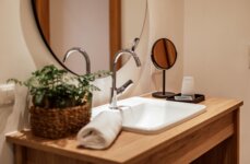 Modern bathroom sink with a round mirror, potted plant, and rolled towel on a wooden counter.