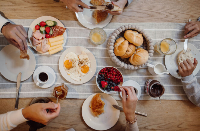 Reich gedeckter Frühstückstisch mit Spiegeleiern, Semmeln, Croissants, Aufschnitt, Käse, Beeren, Kaffee und Saft.