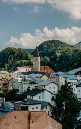 Stadtansicht von Hallein, umgeben von grünen Hügeln und einer Kirche mit Uhrturm im Zentrum unter blauem Himmel.