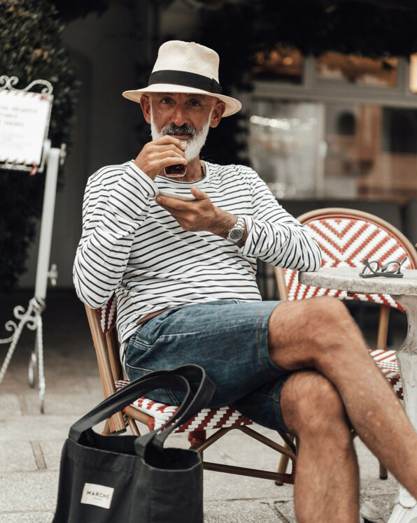 Ein Mann sitzt in einem Café, trägt einen Hut und genießt ein Getränk.