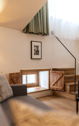 Cozy interior with wooden steps, small window, green curtains, and a framed photo on the wall, reflecting a warm and inviting atmosphere.