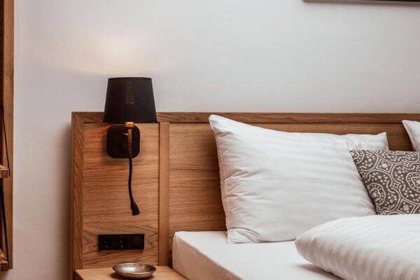 Holzbett in stilvoll gestaltetem Zimmer mit Nachttisch, Lampe und Bild an der Wand.