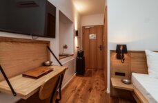 Gemütliches Hotelzimmer mit Holzinterieur, Schreibtisch, Fernseher und Koffer. Elegantes Ambiente und warme Beleuchtung.