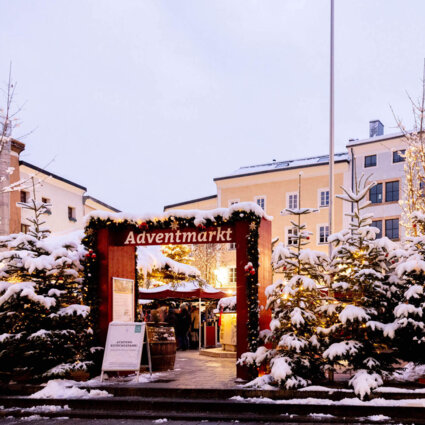 Ein Adventmarkt in Hallein, umgeben von schneebedeckten Tannenbäumen, lädt zu einem gemütlichen Besuch ein.