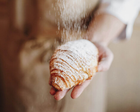 Baker dusts a fresh croissant with powdered sugar.