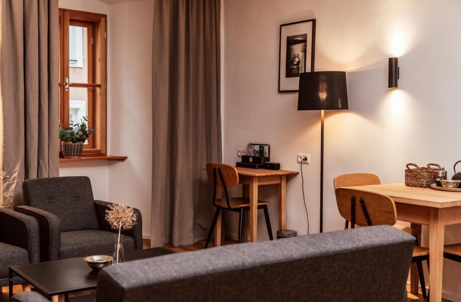 Gemütliches Wohnzimmer eines Apartments mit grauen Sitzmöbeln, Holztisch mit Stühlen und dezenter Beleuchtung.