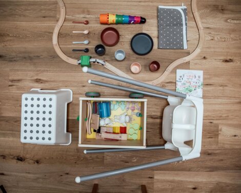 Children's play area with toys, wooden train tracks, colorful kitchenware, and a storage box on a wooden floor.