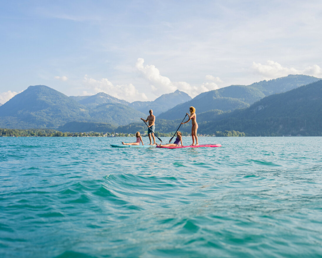 Eine Familie genießt Stand-Up-Paddling auf einem malerischen See, umgeben von Bergen.