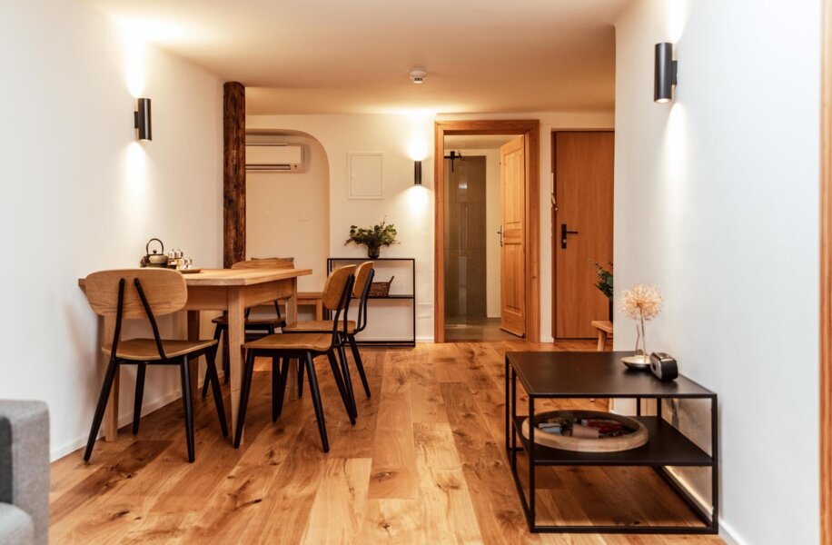 Modern dining area with wooden floors, a table and chairs, and soft lighting, a hallway leads to a wooden door.