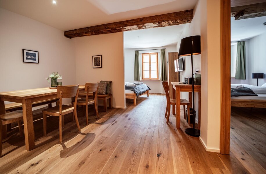 Apartment mit Wohnbereich und zwei Schlafzimmern mit Holzboden, Esstisch, Stühlen und einem Schreibtisch.