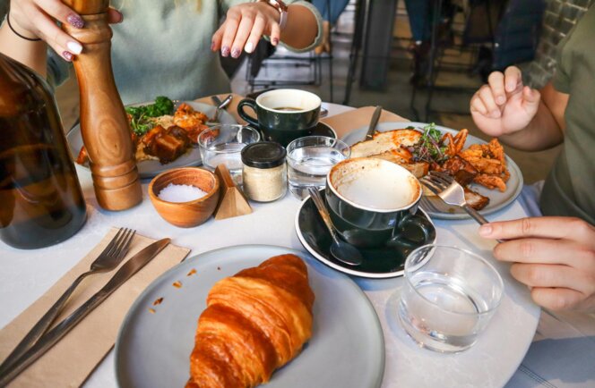 Brunch mit Croissant, Kaffee und herzhaften Tellern, zwei Gäste essen gemeinsam am Tisch.