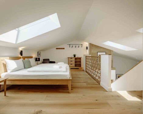 Schlafzimmer im Galerie-Apartment mit Holzboden, modernem Bett, großer Fensterfront und heller Einrichtung.