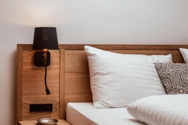 Holzbett in stilvoll gestaltetem Zimmer mit Nachttisch, Lampe und Bild an der Wand.