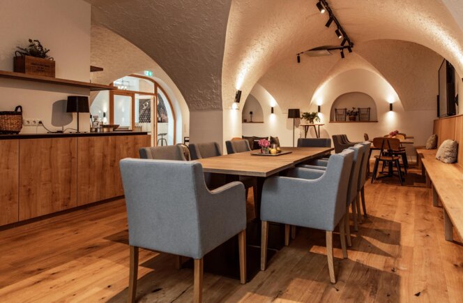 Veranstaltungsraum "Salzkammer" mit Holzboden, gewölbter Decke, großem Tisch und grauen Stühlen. Gemütliche Beleuchtung und Dekoration.
