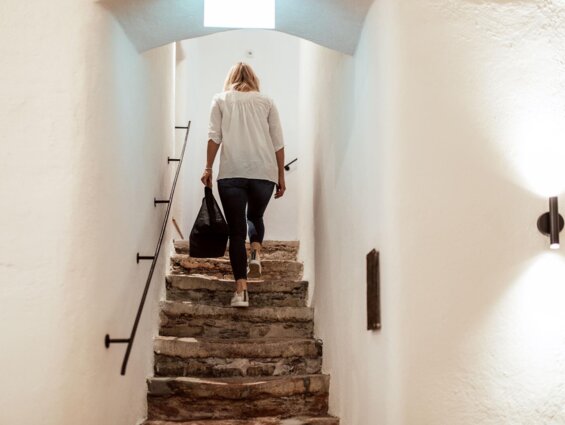 Eine Person steigt eine steinerne Treppe in einem hellen Stiegenhaus hinauf.